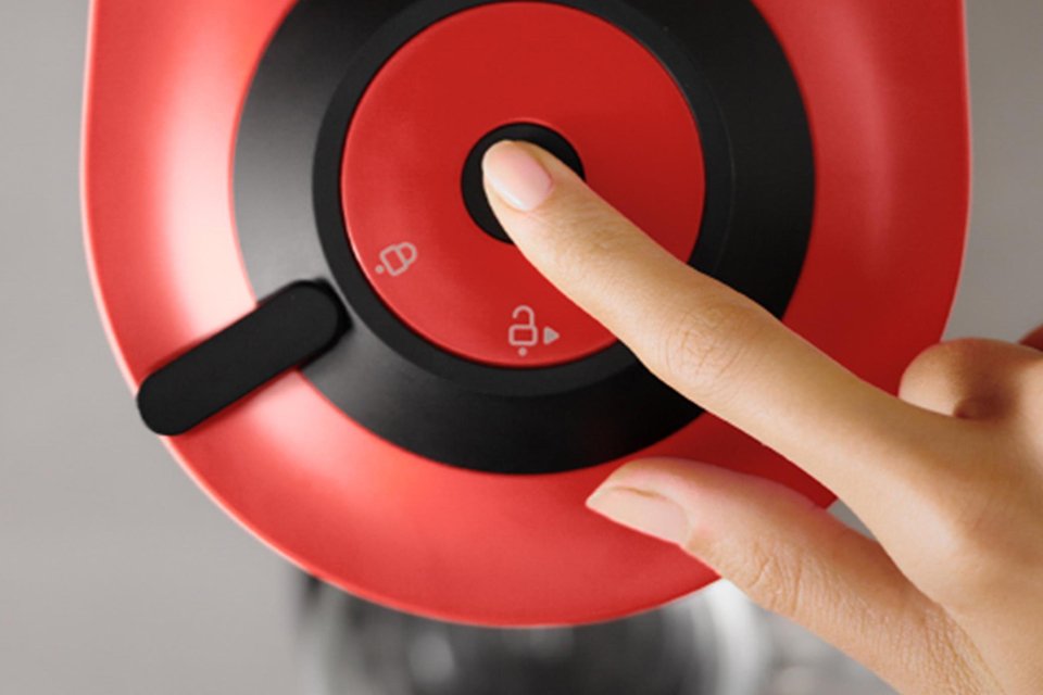 A finger pressing the button on top of a Nespresso Vertuo coffee machine.